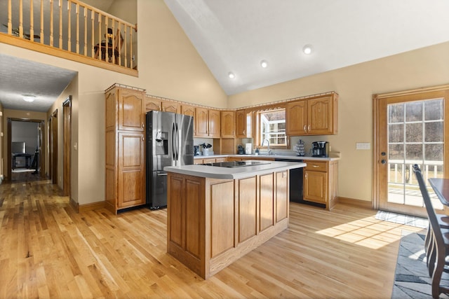 kitchen with a center island, light countertops, light wood-type flooring, stainless steel refrigerator with ice dispenser, and a sink