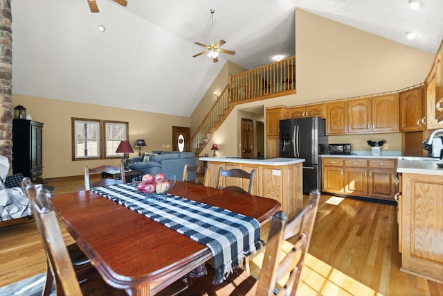 dining space featuring ceiling fan, high vaulted ceiling, stairs, and light wood-style floors