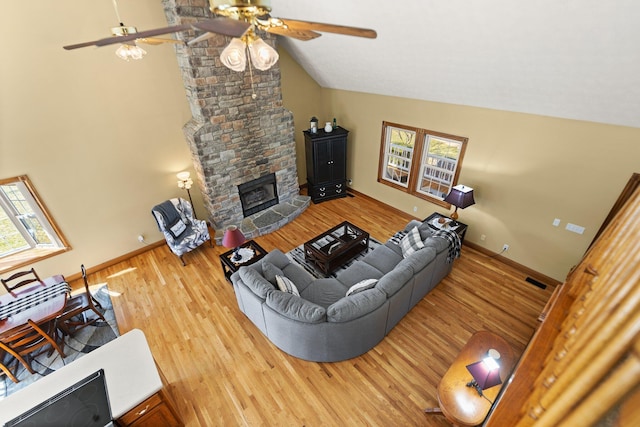 living room with vaulted ceiling, a stone fireplace, and wood finished floors