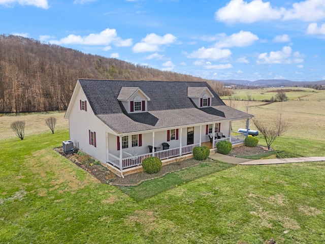 country-style home featuring central air condition unit, covered porch, a shingled roof, and a front yard