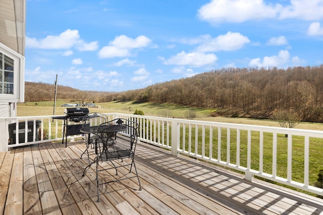 wooden deck featuring a forest view, outdoor dining area, and a lawn