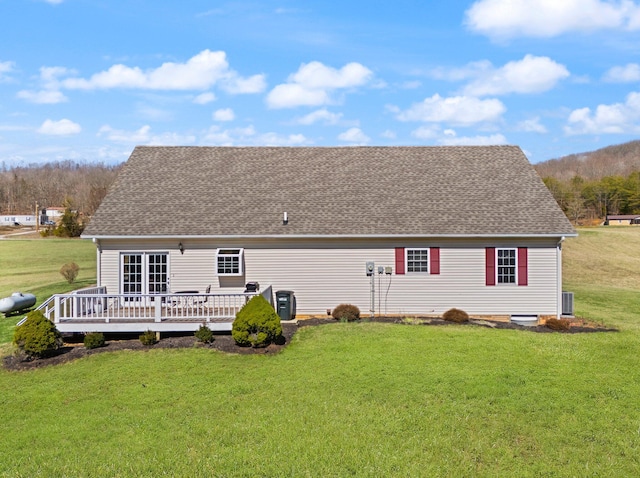 rear view of property featuring roof with shingles, a deck, and a yard