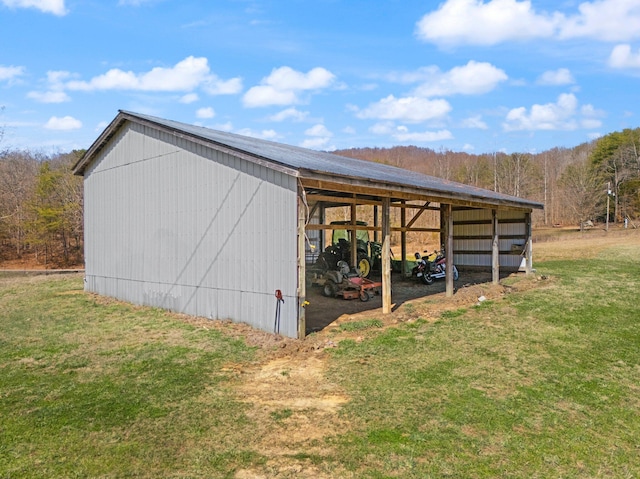 view of pole building with a carport, a lawn, and a wooded view