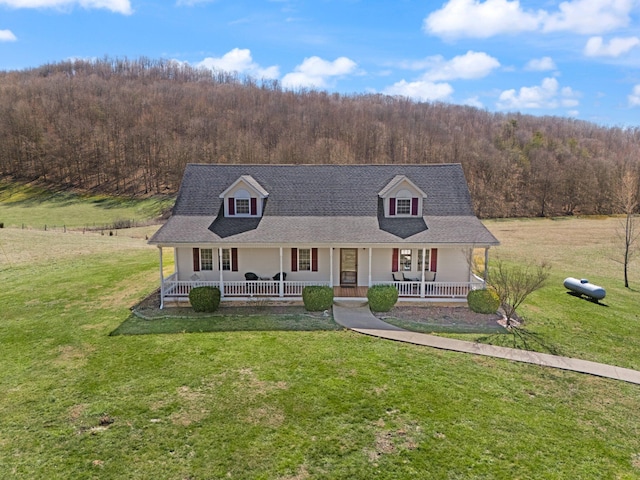 view of front of house with a forest view, a porch, a front lawn, and roof with shingles