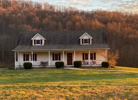 cape cod home featuring a porch, a front yard, and a view of trees