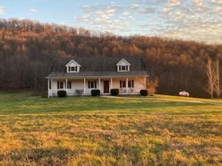 view of front of property with a porch, a view of trees, and a front yard