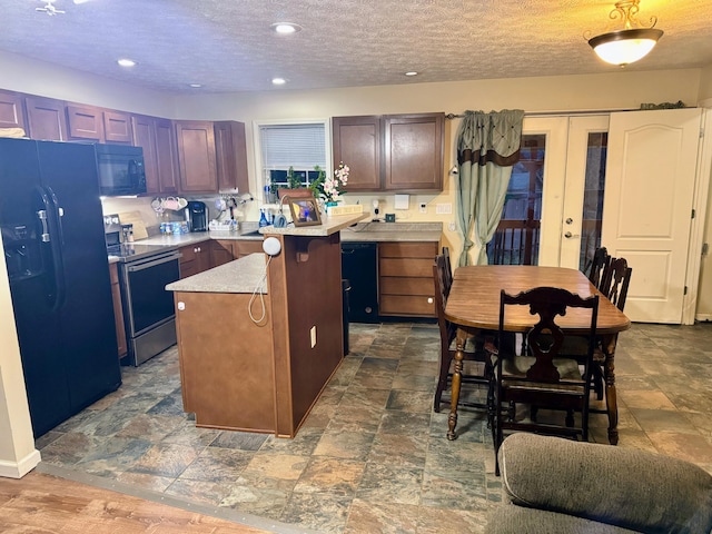 kitchen featuring a textured ceiling, recessed lighting, a kitchen island, light countertops, and black appliances