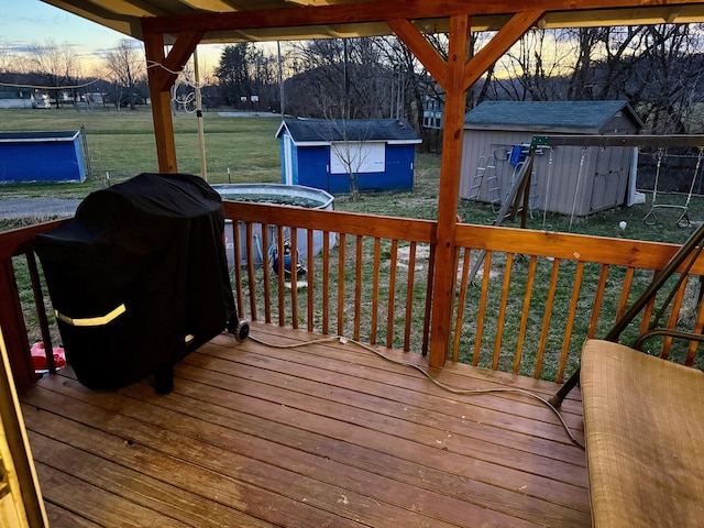 deck at dusk featuring a storage shed, a lawn, area for grilling, and an outdoor structure