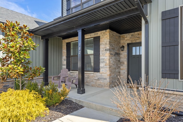 doorway to property with a porch, stone siding, a shingled roof, and board and batten siding