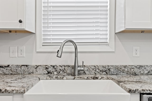 details featuring light stone counters, white cabinets, and a sink