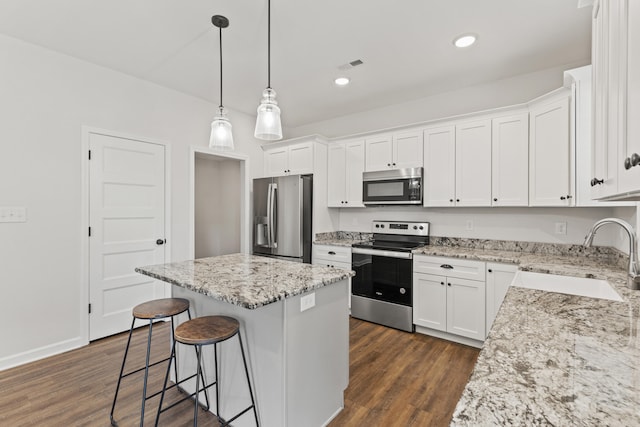 kitchen featuring dark wood finished floors, appliances with stainless steel finishes, a center island, a kitchen bar, and a sink