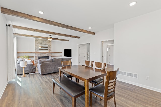 dining room with a fireplace, wood finished floors, visible vents, baseboards, and beamed ceiling