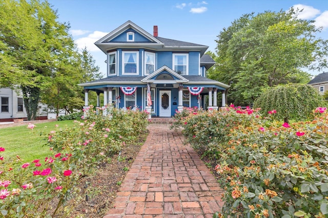 victorian-style house featuring covered porch, a chimney, and a front yard