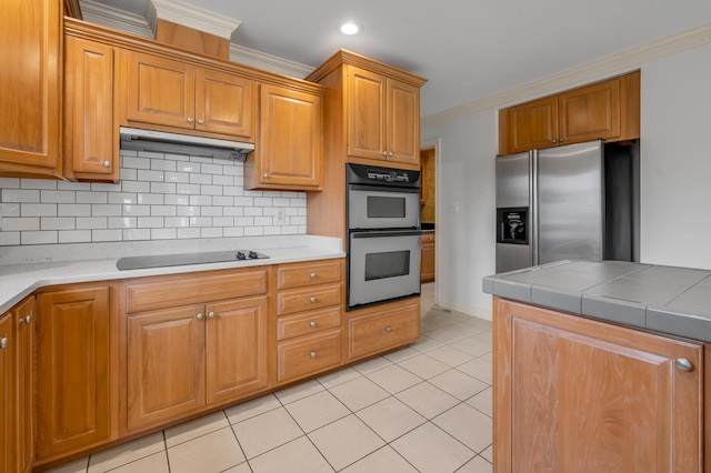 kitchen featuring light tile patterned floors, stainless steel appliances, tasteful backsplash, ornamental molding, and under cabinet range hood