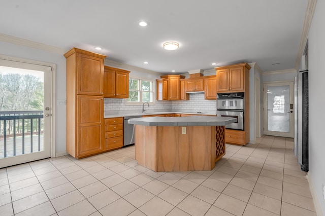 kitchen with light tile patterned floors, stainless steel appliances, ornamental molding, tile counters, and a center island