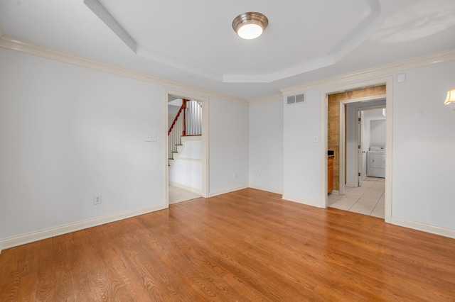 spare room featuring a tray ceiling, washer / clothes dryer, visible vents, and light wood-style floors