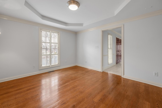 unfurnished room featuring a tray ceiling, light wood-type flooring, and baseboards