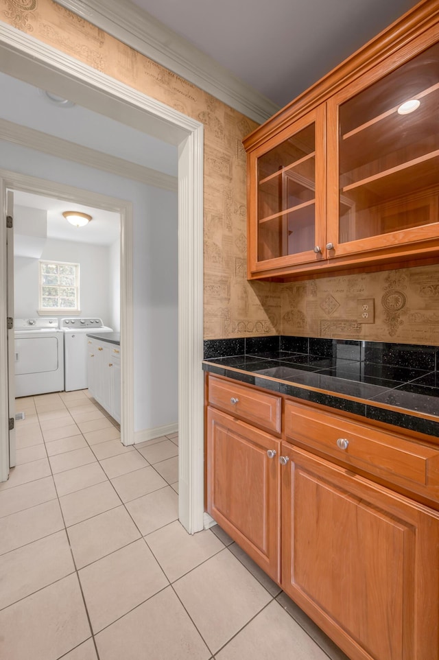 kitchen featuring washer and clothes dryer, glass insert cabinets, brown cabinets, crown molding, and light tile patterned flooring