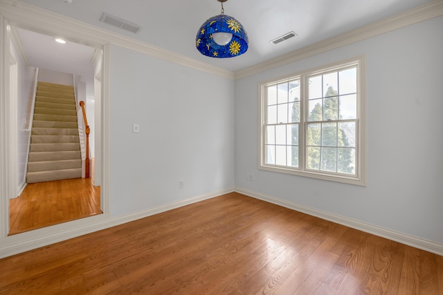 empty room featuring stairs, ornamental molding, wood finished floors, and visible vents