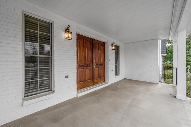 view of exterior entry featuring a porch and brick siding