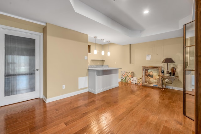 interior space with baseboards, a raised ceiling, and wood finished floors