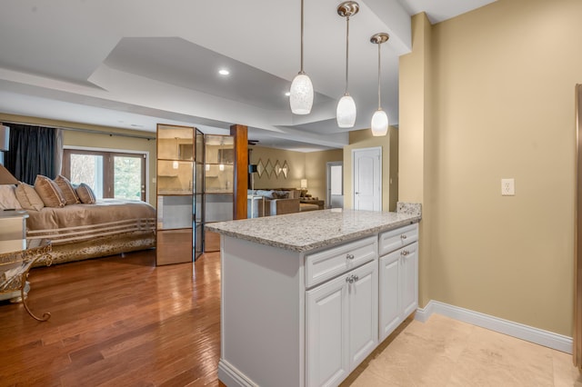 kitchen with a tray ceiling, open floor plan, white cabinetry, light stone countertops, and baseboards