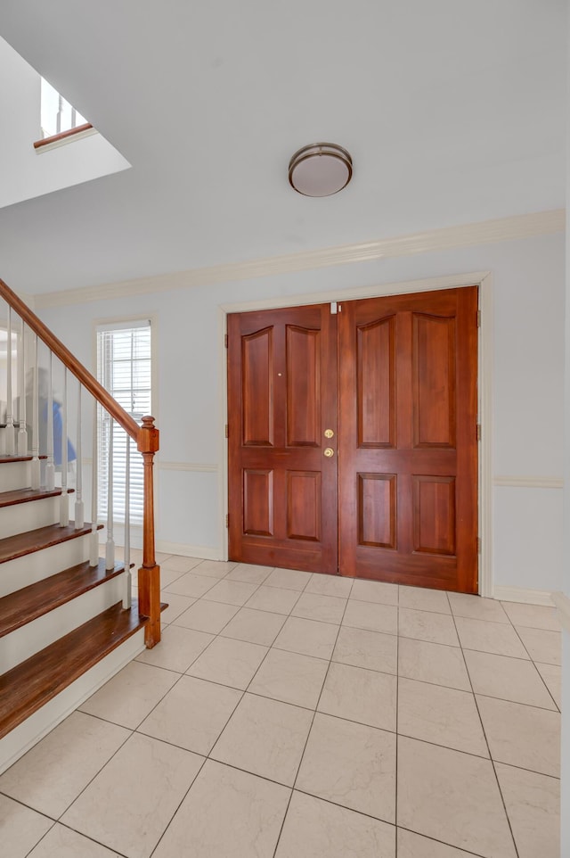 foyer entrance with light tile patterned floors, a skylight, baseboards, stairway, and crown molding