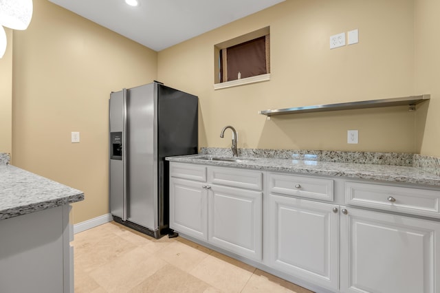 kitchen featuring light stone counters, stainless steel refrigerator with ice dispenser, white cabinets, a sink, and baseboards