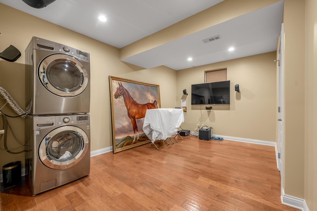 laundry area featuring laundry area, baseboards, visible vents, stacked washer and clothes dryer, and wood finished floors