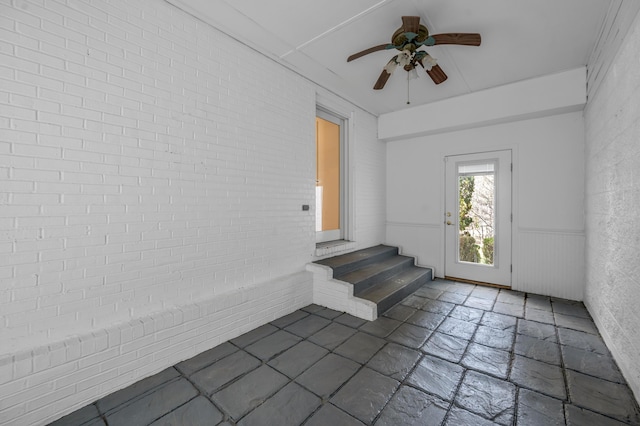 foyer featuring brick wall, wainscoting, stone tile flooring, and a ceiling fan