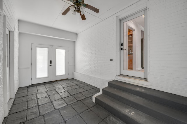 foyer featuring wainscoting, brick wall, ceiling fan, stone finish flooring, and french doors