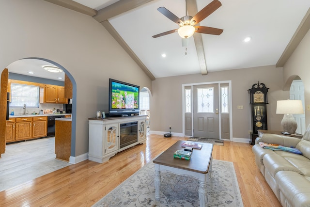 living room with a healthy amount of sunlight, light wood-type flooring, arched walkways, and beam ceiling