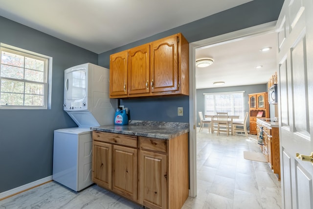 clothes washing area featuring stacked washing maching and dryer, baseboards, marble finish floor, and cabinet space