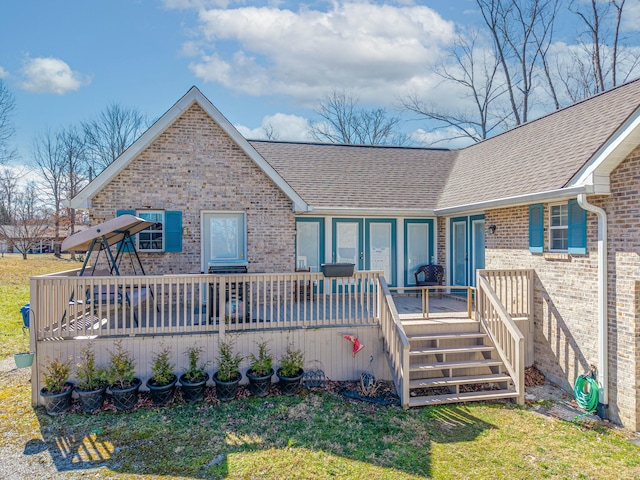 exterior space featuring a shingled roof, a front yard, a wooden deck, and brick siding