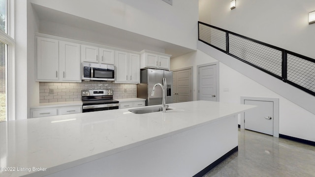 kitchen with white cabinets, a high ceiling, stainless steel appliances, light countertops, and a sink