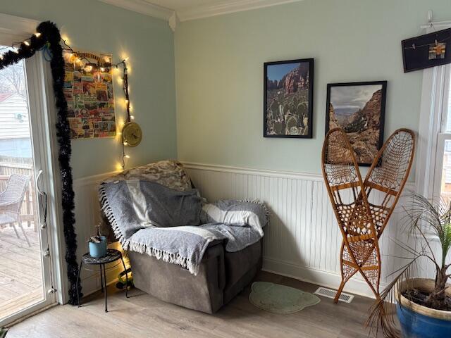 sitting room with a wainscoted wall, wood finished floors, visible vents, and crown molding