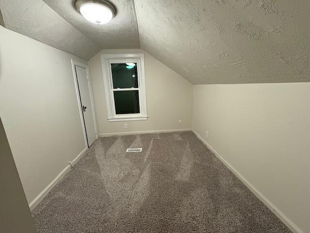 bonus room featuring a textured ceiling, lofted ceiling, carpet floors, visible vents, and baseboards