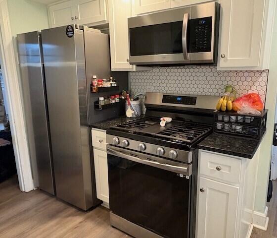 kitchen with light wood finished floors, backsplash, appliances with stainless steel finishes, white cabinets, and dark stone counters