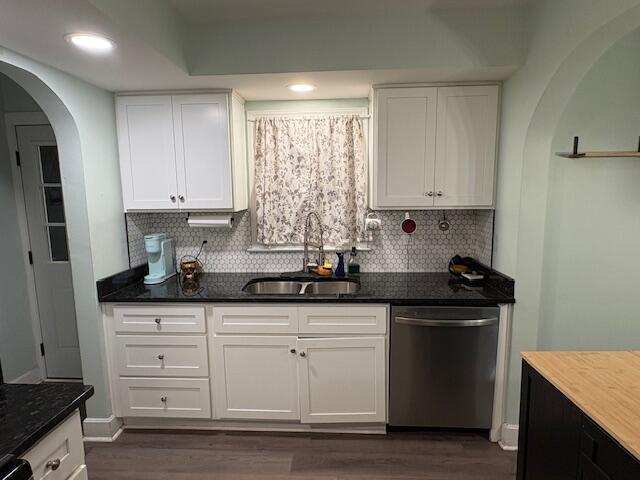 kitchen with arched walkways, white cabinetry, a sink, and stainless steel dishwasher