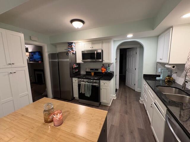 kitchen with arched walkways, appliances with stainless steel finishes, dark wood-type flooring, white cabinetry, and a sink