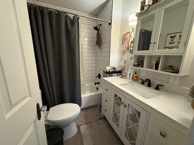 full bathroom with shower / tub combo with curtain, vanity, toilet, and a textured ceiling