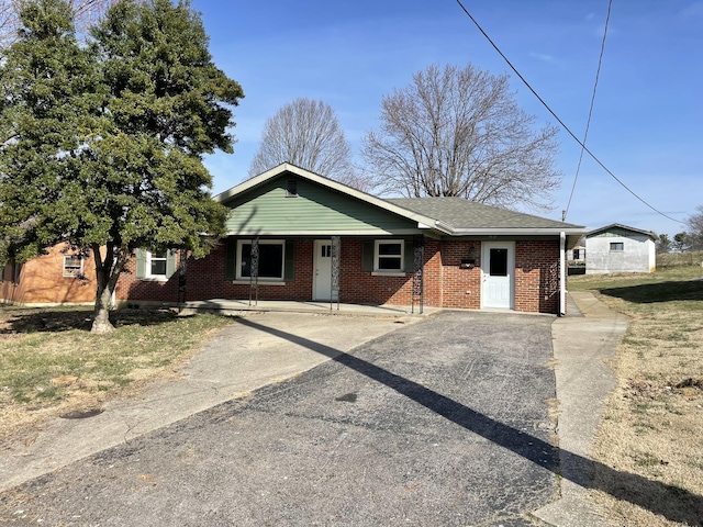 view of front of house featuring a shingled roof, covered porch, brick siding, and driveway