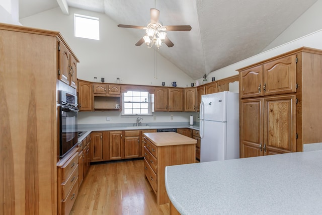 kitchen with light wood finished floors, freestanding refrigerator, light countertops, a sink, and black oven