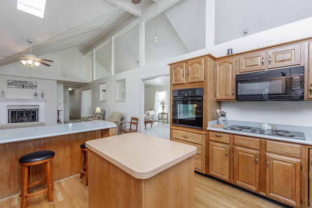 kitchen featuring a center island, light countertops, a brick fireplace, ceiling fan, and black appliances