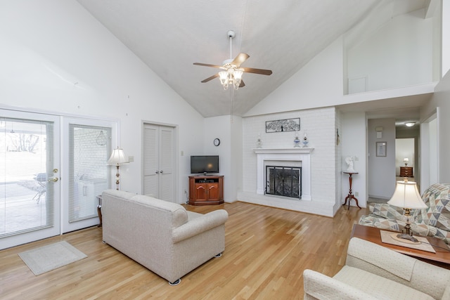 living room with high vaulted ceiling, a fireplace, a ceiling fan, light wood-style floors, and french doors