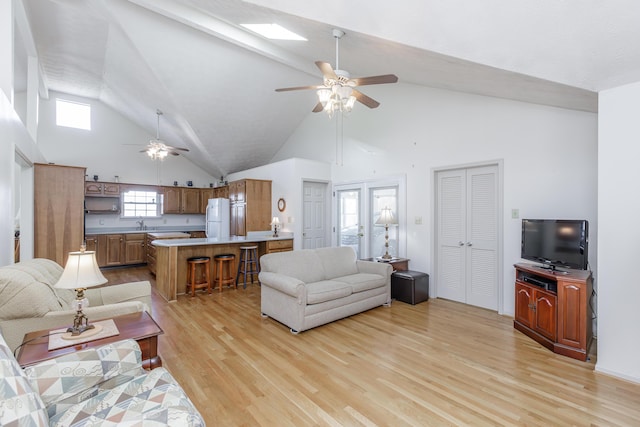 living area with light wood finished floors, ceiling fan, a skylight, and high vaulted ceiling