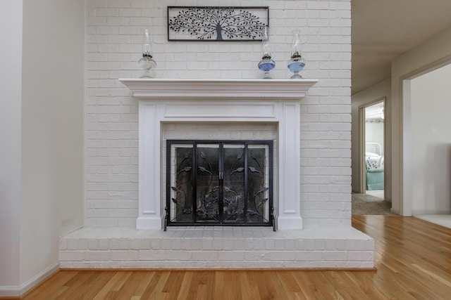 room details featuring a brick fireplace, wood finished floors, and baseboards