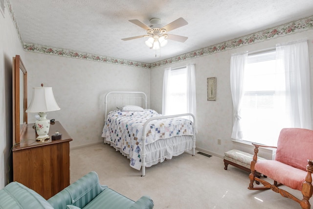 carpeted bedroom featuring a ceiling fan, visible vents, baseboards, and a textured ceiling