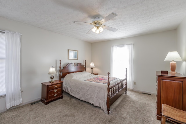 bedroom with baseboards, a textured ceiling, visible vents, and light colored carpet