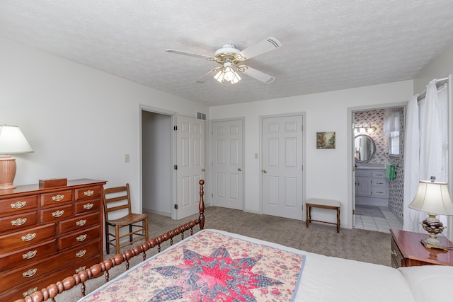 carpeted bedroom with visible vents, ceiling fan, a textured ceiling, and ensuite bath